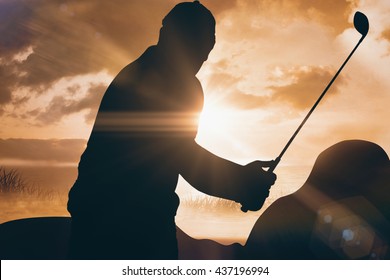 Golf player taking a shot against sunrise over grass