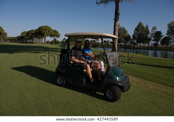 golf\
players driving cart at course on beautiful morning sunrise.\
friends together have fun and relax on\
vacation.