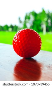 Golf red ball on a wooden surface, green field and blue sky. Macro view, luxury sport concept.
