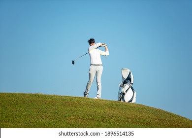 Golfer Asia Man Approach On Tee Off For Swing And Hitting Golf Ball On Slope Green And Looking Fairway In Course. Hobby Playing Game Golf In Holiday And Vacations Day On Club Golf.  Lifestyle Concept