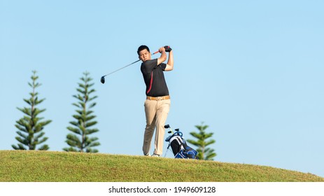 Golfer Asian Man Approach On Tee Off For Swing And Hitting Golf Ball On Slope Green And Looking Fairway In Course. Hobby Playing Game Golf In Holiday And Vacations Day On Club Golf.  Lifestyle Sport 
