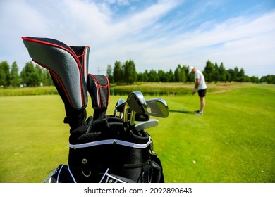 A Golfer With Bag In Sunny Weather Is Preparing To Hit A Chip On The Green At A Golf Course During A Tournament Or Practice. A Bag With Keys In That Pure Iron Stands In The Foreground.