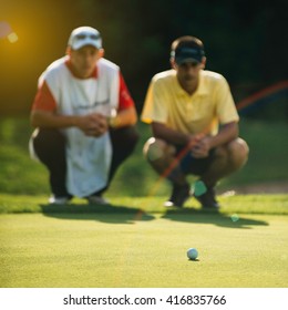 Golfer And Caddy Reading Green. Golf Ball In Focus, Toned Image