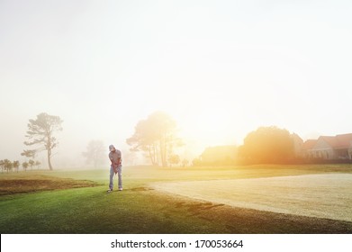 Golfer chipping onto the green at sunrise on the golf course in misty conditions