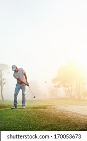 Golfer Chipping Onto The Green At Sunrise On The Golf Course In Misty Conditions