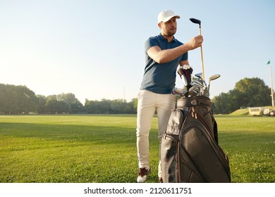 Golfer choosing putter before playing golf on green lawn at sunny day. Concept of entertainment, recreation, leisure and hobby outdoors. Young caucasian man wearing cap, t-shirt, pants and shoes - Powered by Shutterstock