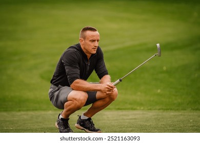 A golfer crouches on the green, holding his putter, deeply focused as he prepares for a putt on a bright golf course. - Powered by Shutterstock