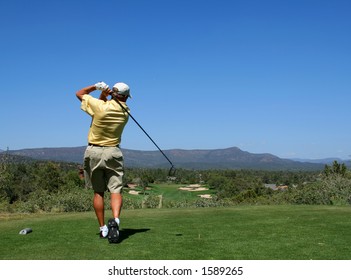 Golfer driving golf ball on beautiful golf course with clear blue sky in the mountains