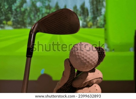 Golfer in glove holds golf ball and club indoors. Playing golf on a simulator