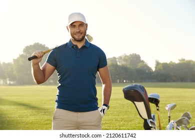 Golfer With Hand In Pocket Holding Putter During Playing Golf On Green Lawn At Warm Sunny Day. Concept Of Entertainment, Recreation, Leisure And Hobby Outdoors. Young Caucasian Man Looking At Camera