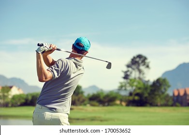 Golfer hitting golf shot with club on course while on summer vacation
