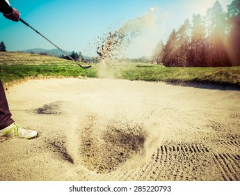 Golfer hitting out of a sand trap. The golf course is on the sand. Sand making splashes. Sun and sunshine in the background