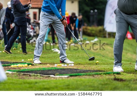 Golfer legs at golf tournament practice swing with golf club. Golf players on green lawn putting golf ball in the hole. Golfing competition or tournament.