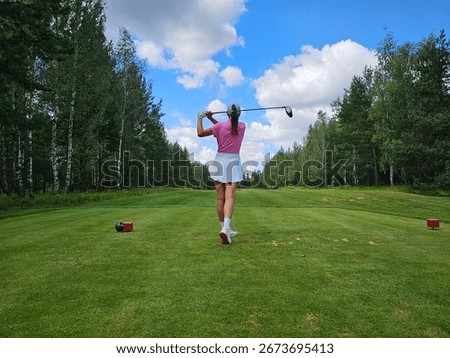 Golfer preparing to tee off in a lush green forested golf course under a partly cloudy sky