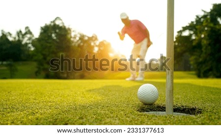 Golfer putting ball on the green golf, lens flare on sun set evening time. Golfer action to win after long putting golf ball in to the hole.                               