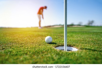 Гольфист кладет мяч для гольфа на зеленый гольф, блики на солнце заходят в вечернее время. Профессиональное поле для гольфа на закате, во время восхода солнца.

