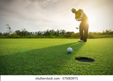 Гольфист кладет мяч для гольфа на зеленый гольф, блики на солнце заходят в вечернее время.