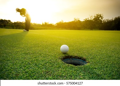 Golfer putting golf ball on the green golf, lens flare on sun set evening time. - Shutterstock ID 575004127