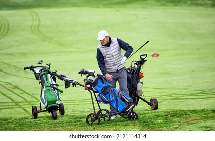 The golfer removes a golf club from the bag and heads for the ball in the fairway. Golfer on a golf course in winter with cart tracks in the wet grass. - Powered by Shutterstock