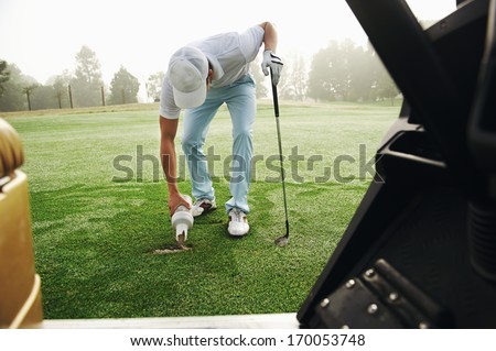 Golfer repairing divot by filling with sand on the fairway