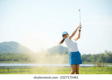 Golfer sport course golf ball fairway. People lifestyle woman playing game golf and hitting go on green grass river and mountain background.  Asia female player game shot in summer.  Healthy Sport