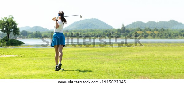Golfer sport course golf ball fairway. People
lifestyle woman playing game golf and hitting go on green grass
river and mountain background.  Asia female player game shot in
summer. copy space
banner