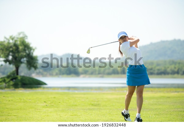 Golfer sport course golf ball fairway. People\
lifestyle woman playing game golf and hitting go on green grass\
river and mountain background.  Asia female player game shot in\
summer.  Healthy  Sport