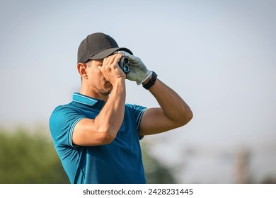 Golfer using a rangefinder to measure the distance to the hole holding it to his eye as he peers down the fairway in a close up head and shoulders for a healthy active lifestyle or sport concept. - Powered by Shutterstock