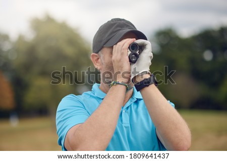 Golfer using a rangefinder to measure the distance to the hole holding it to his eye as he peers down the fairway in a close up head and shoulders for a healthy active lifestyle or sport concept