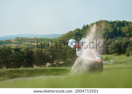 Golfers exploding sand in the bunker.	
