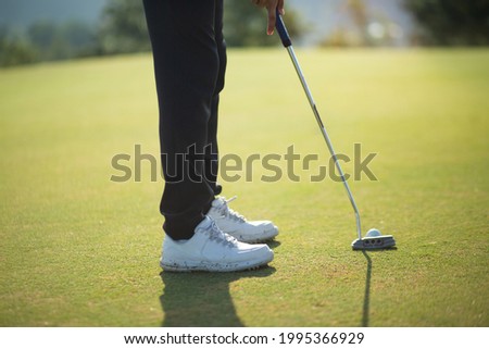Golfer's feet who are putting golf balls on the green in the warm sunshine in the morning.