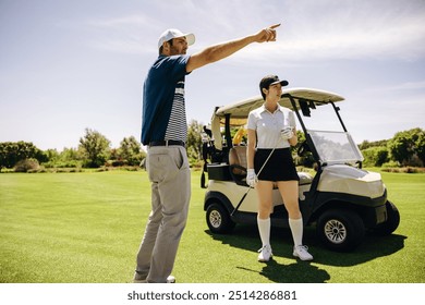 Golfers stand by a golf cart, one pointing while discussing strategy and competition. A bright, sunny day enhances their focus and team planning. - Powered by Shutterstock