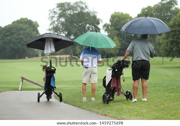 Golfers use\
umbrellas during a rainy round of\
golf