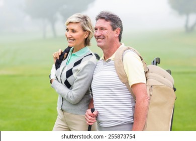 Golfing Couple Smiling And Holding Clubs On A Foggy Day At The Golf Course