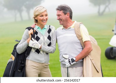 Golfing Couple Smiling And Holding Clubs On A Foggy Day At The Golf Course