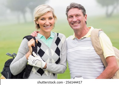 Golfing Couple Smiling And Holding Clubs On A Foggy Day At The Golf Course