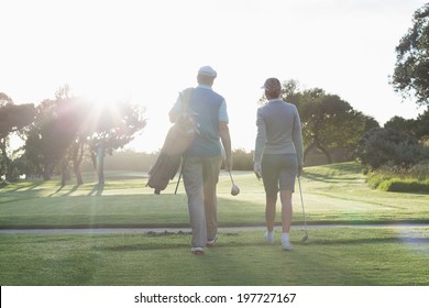 Golfing Couple Walking And Chatting On A Sunny Day At The Golf Course