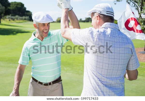 Golfing friends high fiving on the eighteenth\
hole on a sunny day at the golf\
course