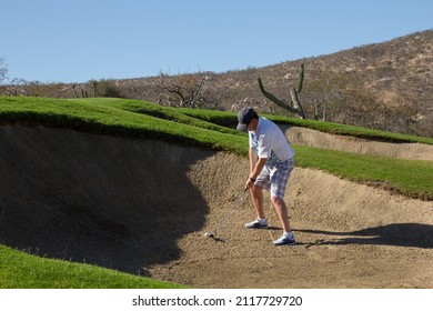 Golfing Middle Aged Man, Getting Ready To Hit Out Of A Deep Bunker. Desert Hill And Deep Blue Clear Sky In Background.