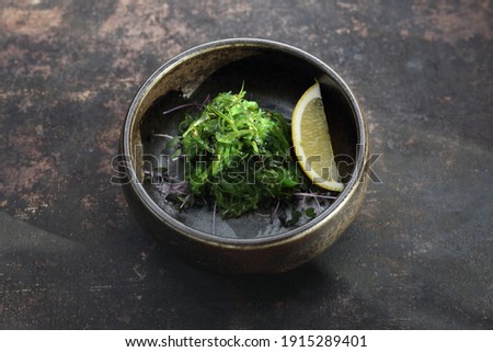 A goma wakame, top view, on a black stony background. A pickled seagrass, seaweed Japanese salad with sesame, decorated with a lemon wedge. A traditional oriental cuisine, sushi restaurant menu.