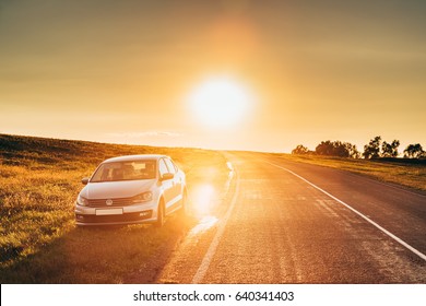 Gomel, Belarus - August 25, 2016: Sun Rising Over VW Volkswagen Polo Vento Sedan Car Parking Near Asphalt Country Road In Sunny Morning Or Evening. Open Road At Sunny Sunset Or Sunrise Time At Summer