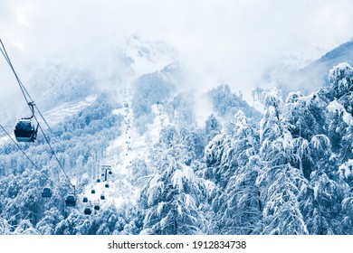 Gondola lift in ski resort in winter mountains during snowfall. Rosa Khutor, Sochi, Russia. Beautiful snow-covered forest, winter landscape