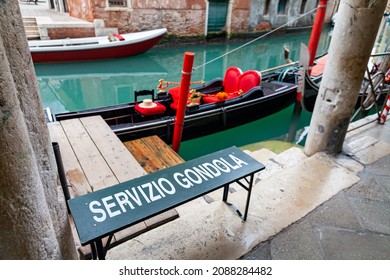 A gondola in Venice with a gondola service sign. An empty gondola waiting for tourists. A gondola next to an ancient portico in Venice, Italy.