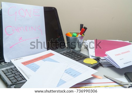 Gone camping note left on computer with a  final demand letter for mortgage arrears on a cluttered untidy desk.