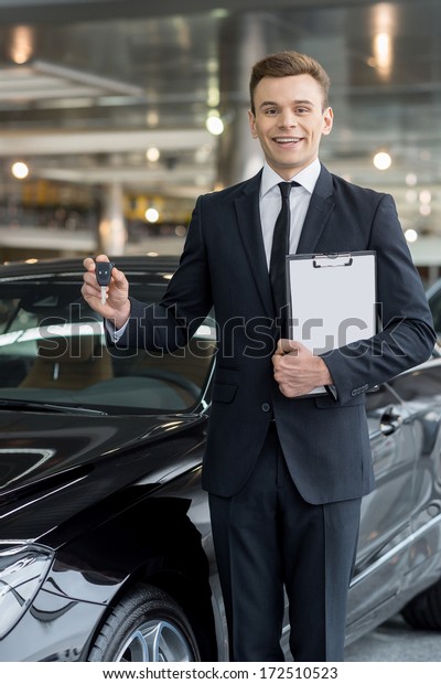 Good choice! Handsome young\
classic car salesman standing at the dealership and holding a\
key