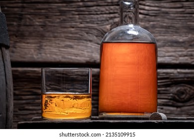 Good Cognac With Bottle In Old Wooden Distillery. Glass Of Bourbon With Ice In An Old Distillery.