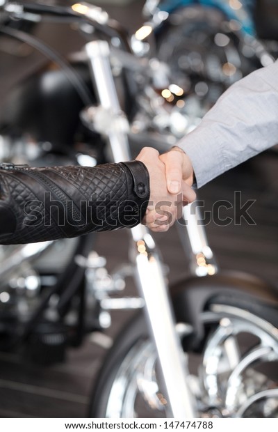 Good deal. Close-up of handshaking with a\
motorcycle on the\
background