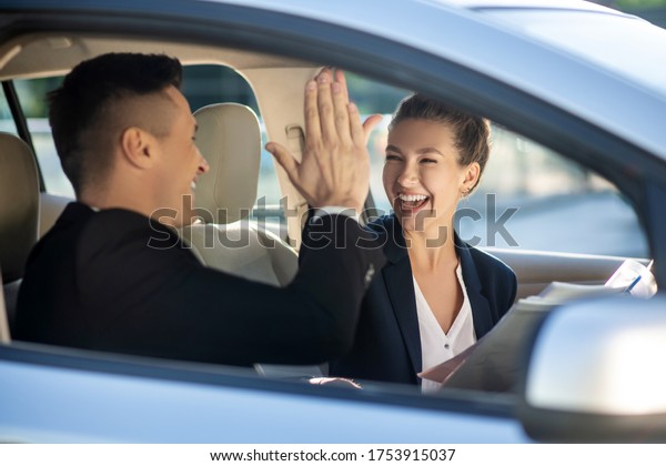 Good deal. Happy\
officially dressed woman and man touching each other with welcoming\
palms in a car, rejoicing