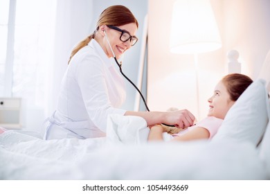 Good Doctor. Optimistic Vigorous Female Doctor Hearing Girl With Stethoscope While Smiling And Looking At Her