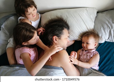 Good Family Morning, The Children Came To Bed To The Sleeping Dad, The Children Play Around The Sleeping Parent. Sunday Morning Or Quarantine Morning